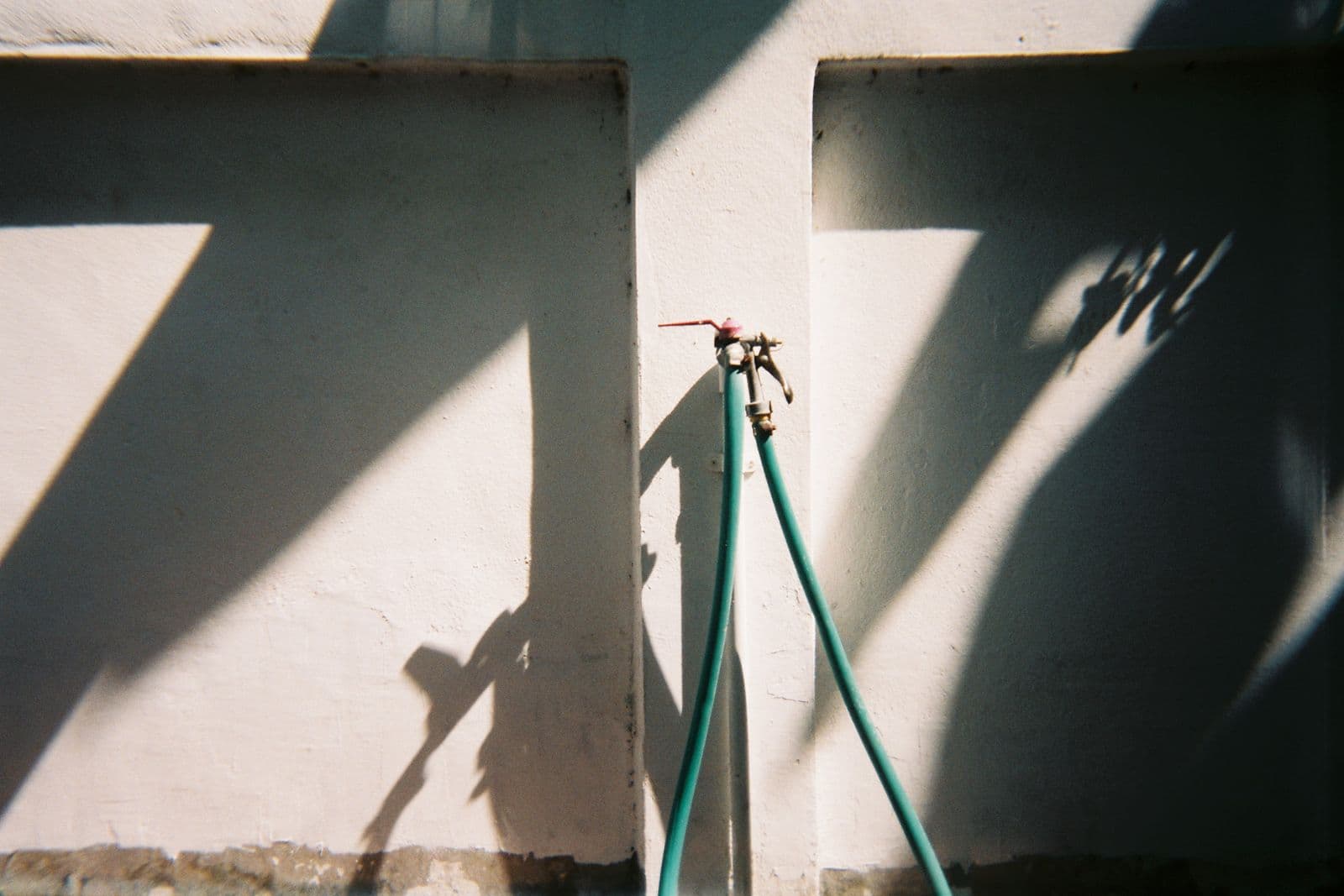 An outdoor water tap with a hose connected, in daylight
