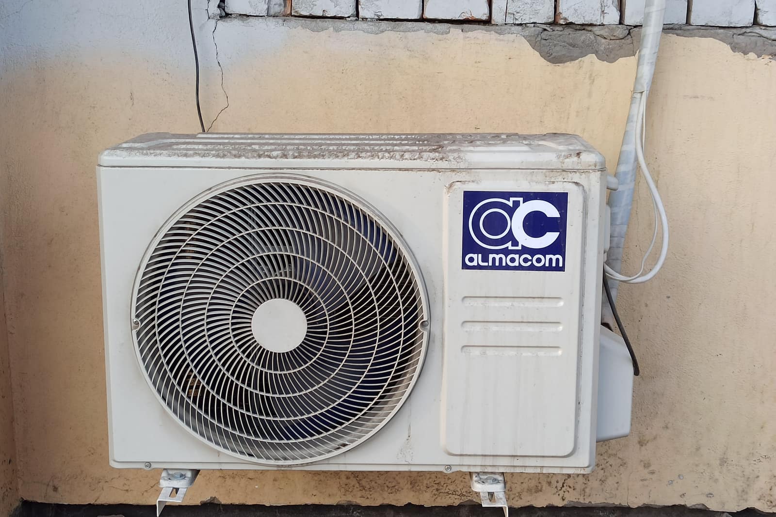 An outdoor air conditioning condenser unit mounted on a brick wall