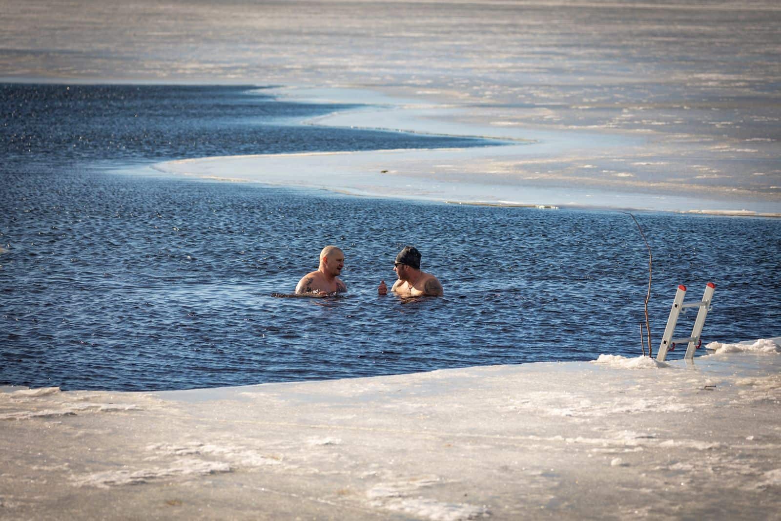 Two people swimming in cold open water in winter